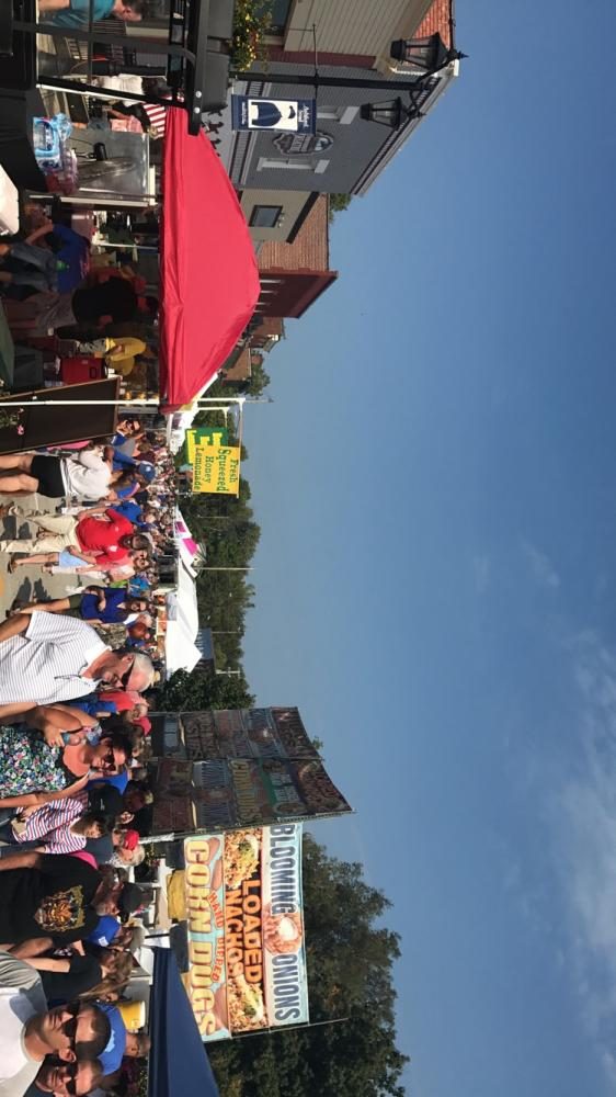 Street shot of the crowd by food vendors, selling items like honey lemonade, kettle corn, funnel cakes, and ice cream.