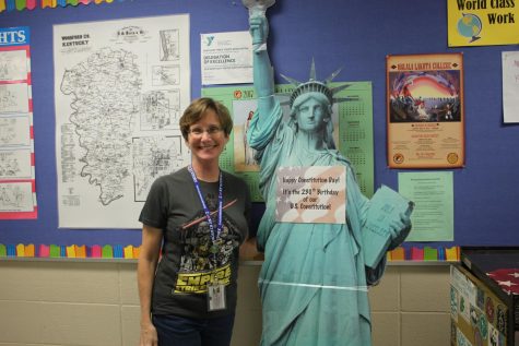 Ms.Finney stands in her room next to the Statue of Liberty. 