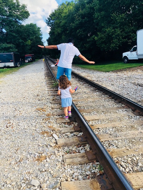 Father entertaining his daughter on the train track to let out some fun.