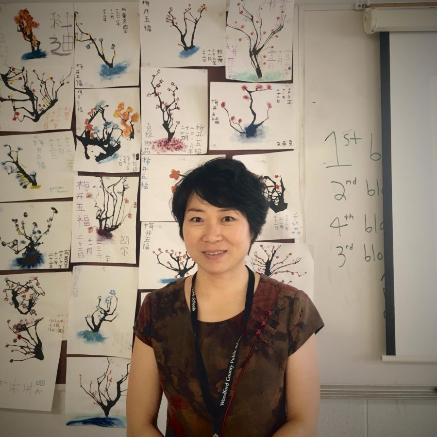 Ms. Wu in front of Chinese calligraphy artwork.
