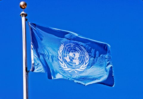 UN Photo taken by John Isacc. The flag of the United Nations, with its white emblem on a light blue field, flies from a pole in front of UN Headquarters in New York.