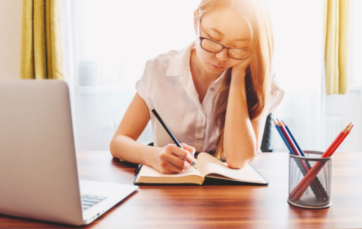 Young woman taking note and using laptop while studying at home