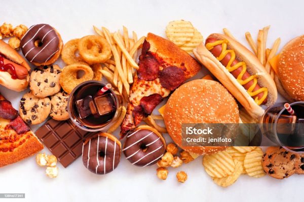 Junk food table scene scattered over a white marble background. Collection of take out and fast foods. Pizza, hamburgers, french fries, chips, hot dogs, sweets. Top view.